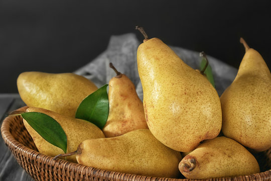 Wicker basket with fresh ripe pears on dark background