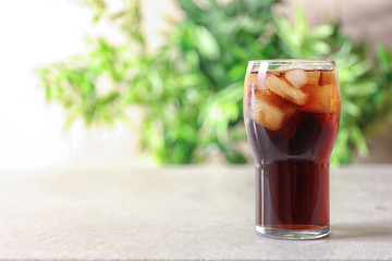 Glass of refreshing cola with ice on table