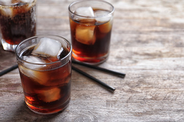 Glasses of refreshing cola with ice on wooden table