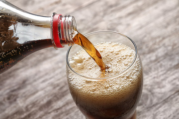 Pouring cola from bottle into glass on wooden background, closeup