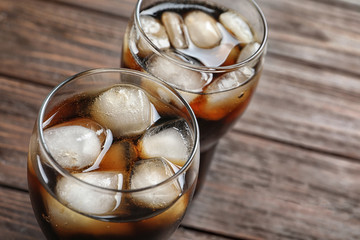 Two glasses of refreshing cola with ice on wooden table, closeup