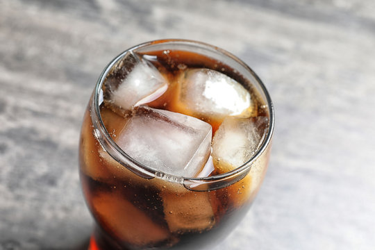 Glass of refreshing cola with ice on table
