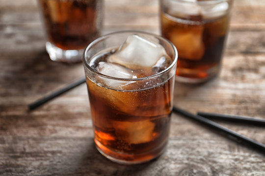 Glass of refreshing cola with ice on wooden table