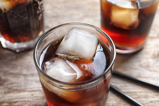 Glass of refreshing cola with ice on wooden table, closeup
