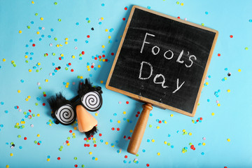 Chalkboard with phrase "Fool's day" and funny glasses on color background. 1st April celebration