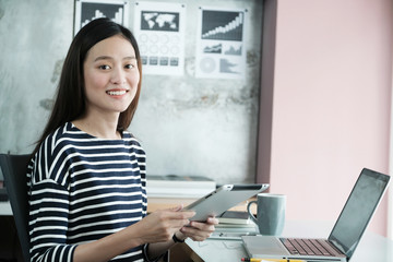 Obraz na płótnie Canvas Young asian businesswoman using tablet with smiling face, positive emotion, at office, casual office life concept