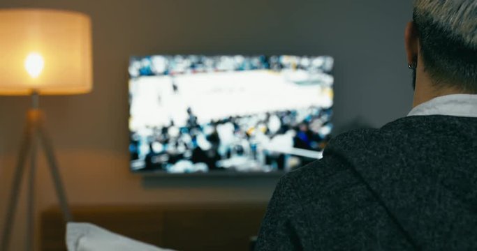 RL DOLLY Back view of Caucasian male sitting on sofa, watching sport basketball game on a TV screen. 4K UHD