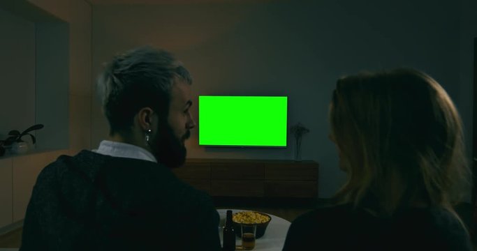 GREEN SCREEN Back view of young adult Caucasian couple sit on couch at home, watching TV. 4K UHD