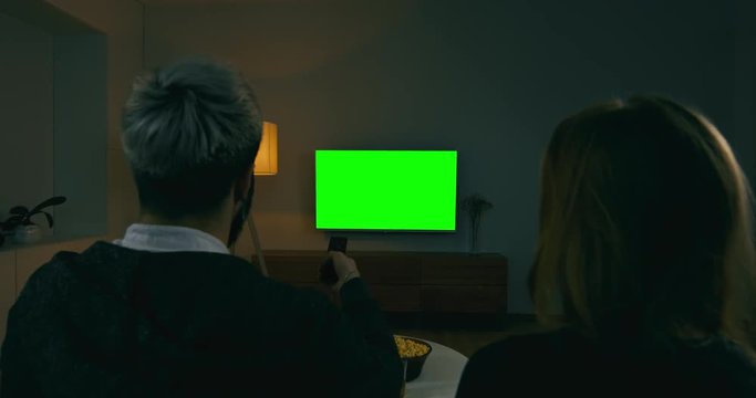 GREEN SCREEN Back view of young adult Caucasian couple sit on couch at home, watching TV. 4K UHD