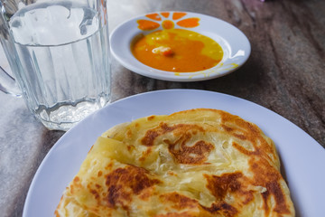 Roti canai and curry sauce on the plate over dining table