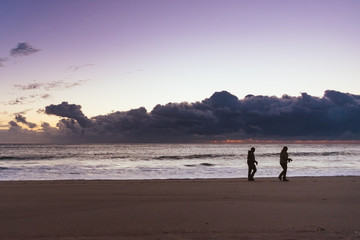 two silhouettes of people walking on the beach at sunrise
