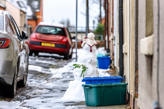 Cloudy winter day view of homemade snowman on typical british road footpath next to empty recycling bin boxes