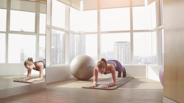 Perfect plank. Full-length side view of young beautiful woman in sportswear doing plank while standing in front of window at gym