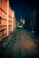 Dark and eerie urban city alley with an old vintage factory warehouse and smokestack at night.