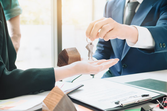 real estate agent holding house key to his client after signing contract agreement in office,concept for real estate, moving home or renting property