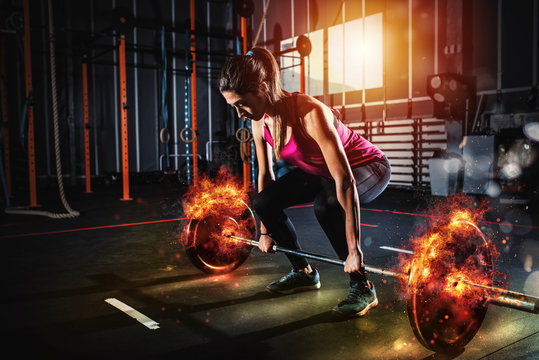 Athletic girl works out at the gym with a fiery barbell