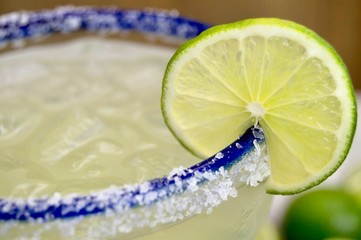 Close up of a salted, blue rimmed margarita glass with lime slice