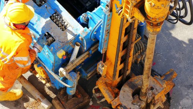 Drilling rig worker dressed in yellow helmet and working clothes operating machinery. Man using the functional buttons and fixing rotary metal pipes for industrial exploration