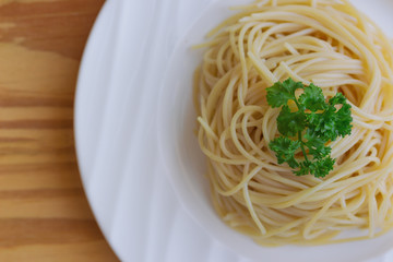 Boiled spaghetti with al dente level. Cooked pasta prepared for cooking on white plate, close up in top view flat lay view with copy space on wood table. Homemade Italian traditional food concept.