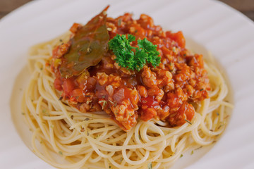 Spaghetti bolognese sauce with beef or pork,cheese,tomatoes and spices on white plate on wood table, top view with close up. Homemade delicious Italian traditional food for lunch or dinner.