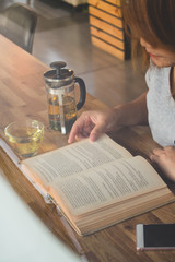 A girl reading a book and holding a cup of tea wit tea pot on table in cafe