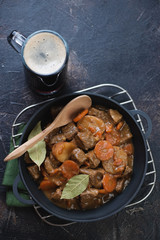 Cast-iron pan with Irish beef and beer stew on a metal cooling rack, high angle view on a dark brown stone background, studio shot