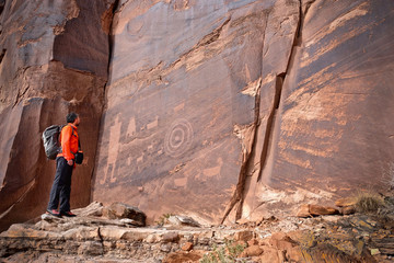 Man looking at rock art of Pueblo Indians. Owl, thunderbird, goat and a man figure petroglyphs on...