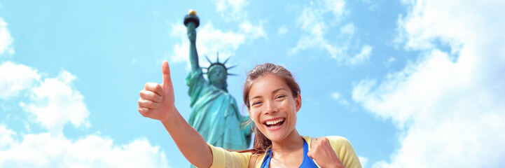 New York City tourist woman at Statue of Liberty happy doing thumbs up banner panorama. Asian girl...