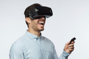 Naklejka premium Young man using vr headset, experiencing virtual reality while playing video game, using remote control with hand