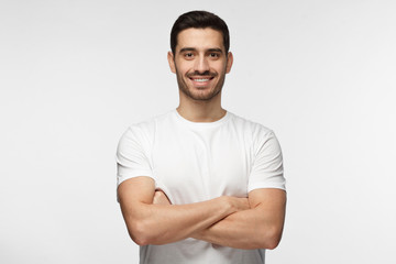 Portrait of smiling handsome man in white t-shirt standing with crossed arms isolated on gray background