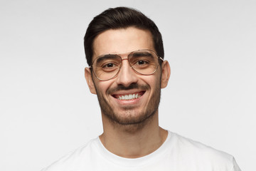 Close up portrait of smiling handsome man in trendy glasses and white t-shirt isolated on light gray background