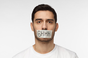 Close up shot of young man with taped mouth with shhh text on it - obrazy, fototapety, plakaty