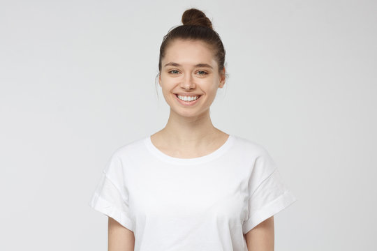Close up portrait of smiling young woman in white t-shirt looking at camera, isolated on gray background