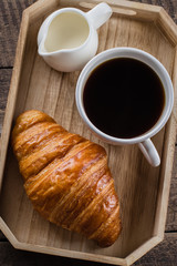 Coffee and croissant for breakfast on rustic wooden tray on table, background. Top view, close up