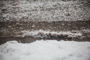 Moody picture of dirty melting snow covering asphalt road.