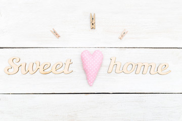 Wooden letters sweet home on a wooden background and a pink heart of a handmade. Flat lay