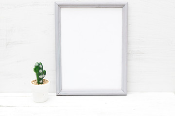 Gray frame and cactus in a pot on a white wooden background. Mininmalist design