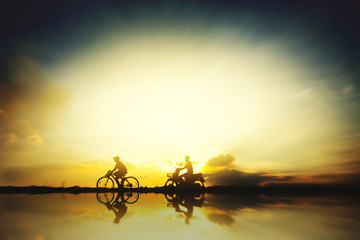 Fototapeta na wymiar Silhouette of a biker and motorcycle driver in sunrise with reflection in water