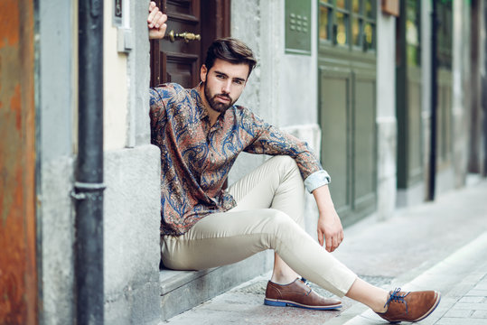 Young bearded man, model of fashion, sitting in an urban step wearing casual clothes.