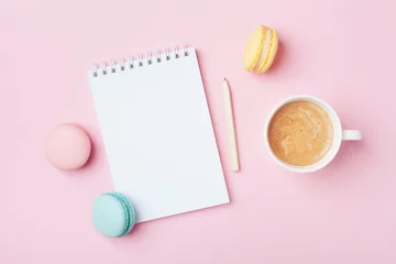 Foto op Canvas Notebook, cup of coffee and colorful macaron on pastel pink desk top view. Cozy morning breakfast. Fashion flat lay. Sweet macaroons. © juliasudnitskaya