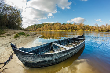 Naklejka na ściany i meble old wooden boat on the bank of a wide river in sunny day