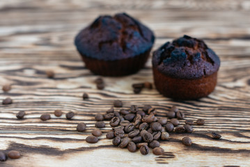 Fresh delicious cupcake and coffee fragrant grains on a wooden background