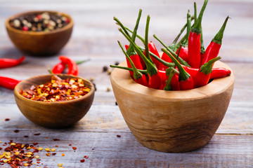 Red hot chilli pepper pods in a wooden mortar, pepper flakes and peppercorns in wooden bowls