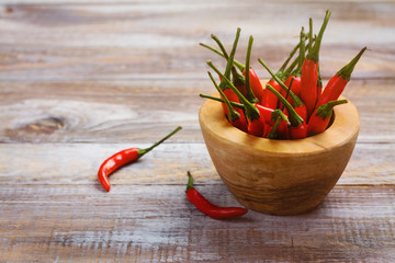 Red hot pepper pods in a wooden mortar and pepper pods on wooden table