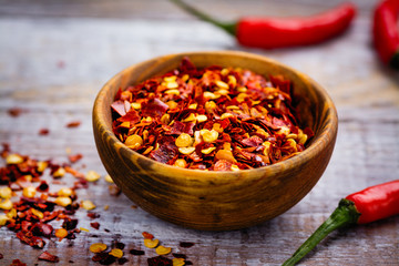 Red hot pepper flakes in a wooden mortar and pepper pods on wooden table