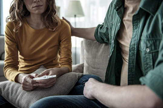 Sad woman holding pregnancy test while sitting near man. Focus on stick with two red strips