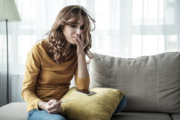 Portrait of depressed young woman holding pregnancy test and crying. Ruined life concept