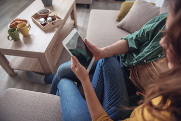 Top view close up of male and female arms holding tablet. Couple is sitting on sofa and hugging