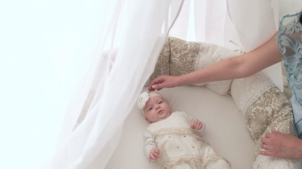 Tracking mother putting baby to sleep while walking . Attractive woman holding baby in hands and walk across living room with bright window curtains in background.