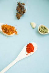 Plastic and glass spoons with dry spices and fresh herbs on a blue background with copy space, top view, close up